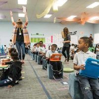 Photo of students working in small groups and also on devices with teachers moving around the room checking in with students