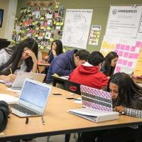 Photo of students seated in groups at multiple tables working