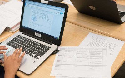 Photo of laptop and hand with papers nearby