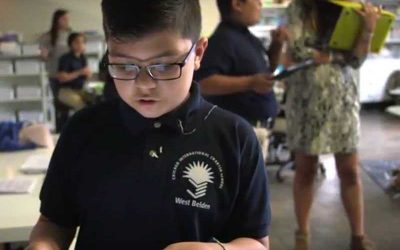 Photo closeup of student working with device with teacher and another student in background