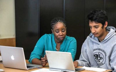 Photo of teacher and student working side by side at table with laptops directly in front of them