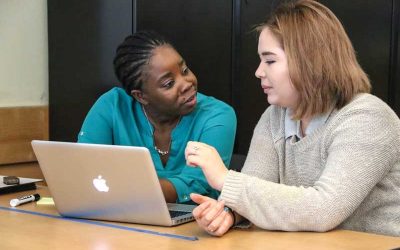Photo of student and teacher working together seated at a table in front of a laptop