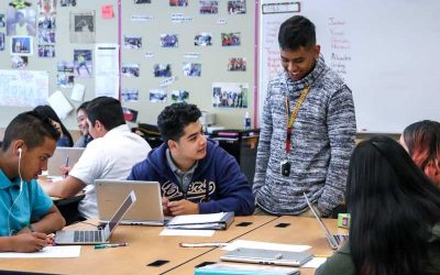 Photo of teacher aide standing at table and speaking with a group of seated students
