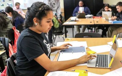 Photo of seated student working with her notebook and on her laptop