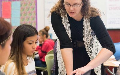 Photo of teacher standing and speaking with individual student seated at desk