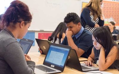 Photo of group of students seated at table working on laptops