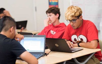 Photo of students working on laptops seated at table