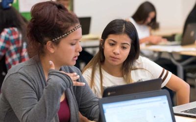 Photo of two students seated with laptops in front having conversation