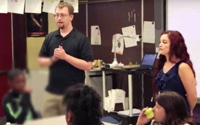 Photo of two teachers standing in front of seated students in a classroom