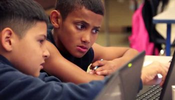 Photo of two students working together on laptops and in conversation