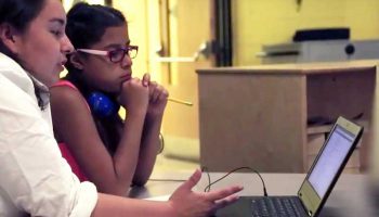 Photo of teacher and student working together at table with laptop