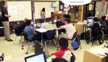 Photo of classroom with indication showing student is signing up for assessment on the whiteboard at front of class