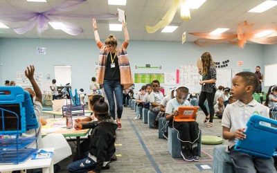 Photo of classroom with students working on devices and teachers roaming classroom