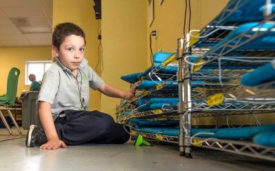 Photo of student seated in front of device storage cart filled with tablet devices