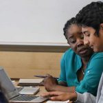 Photo of student and teacher working together seated at a table in front of a laptop