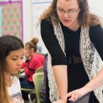 Photo of teacher standing and speaking with individual student seated at desk