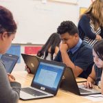 Photo of group of students seated at table working on laptops