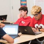 Photo of students working on laptops seated at table
