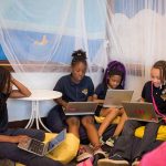Four female students sit on floor, bean bag chairs while working on laptops