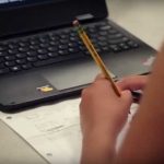 Photo closeup of student working in notebook with laptop on desk