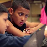 Photo of two students working together on laptops and in conversation