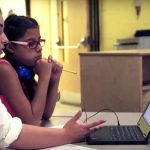Photo of teacher and student working together at table with laptop