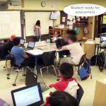 Photo of classroom with indication showing student is signing up for assessment on the whiteboard at front of class