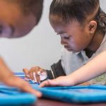 Photo closeup of student working on her tablet device with other students in background