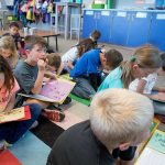 Students sit on floor, looking down and writing in folders