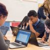 Photo of group of students seated at table working on laptops