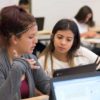Photo of two students seated with laptops in front having conversation