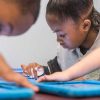 Photo closeup of student working on her tablet device with other students in background