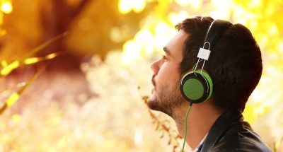 Young man sitting under the tree and listening to music