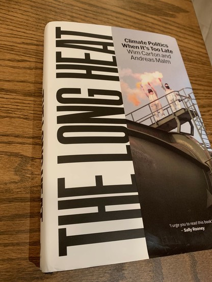 The Long Heat: Climate Politics When It’s Too Late, by Wim Carton and Andreas Malm. The cover shows two masked people holding flares on a catwalk above a large rounded gray metal structure, presumably protestors on a piece of oil infrastructure.