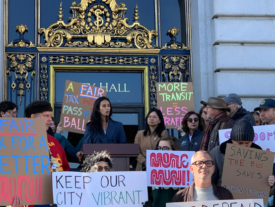 Jackie Fielder speaks on city hall steps amid people with pro transit signs