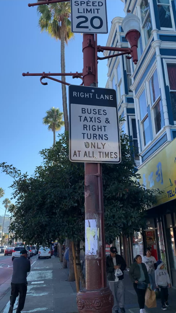 Pans from a sign describing a bus-only lane to the lane, full of double-parked cars