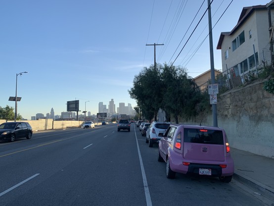 Stroad with four lanes and two parking lanes. LA skyline smeared gray at the horizon.