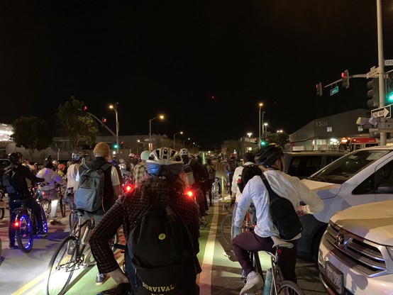 Phalanx of cyclists (facing their backs) at a signal which has just turned green