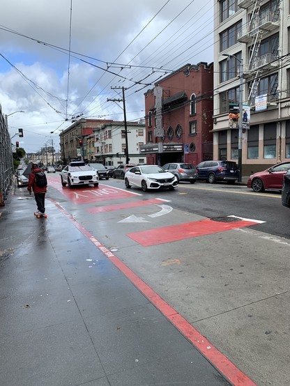 Waymo robotaxi driving in a solid red transit-only lane. Although the lane later becomes dashed red and legal for right-turning cars, the Waymo has clearly entered it before this happens.