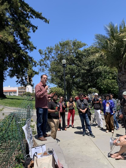 Dean Preston addresses a crowd gathered at the foot of the hill in Dolores Park on a sunny day