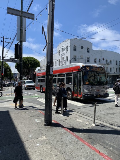 55 bus and a moving van and a line of cars behind them in the intersection on red, pedestrians navigating around to cross.