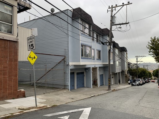 Row of 3-story apartment buildings with ground floor garages along a street.