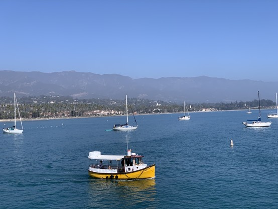 A small white and yellow boat near the coast labeled Lil’ Toot. Hazy mountain ranges run from side to side back from the coast