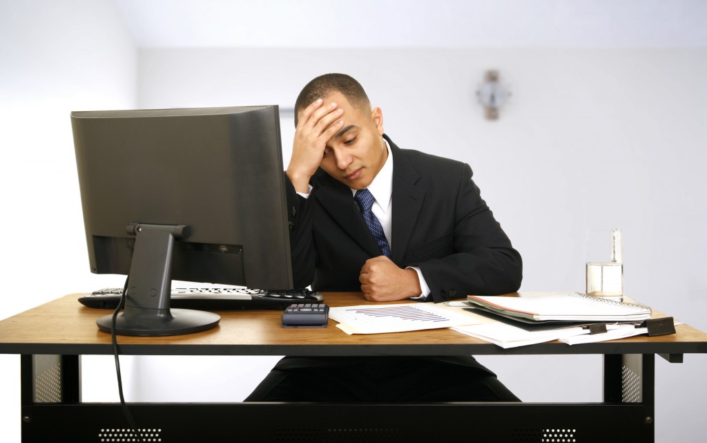 an employee stressed out and still working in his office with a little clock behind him showing a time to get off