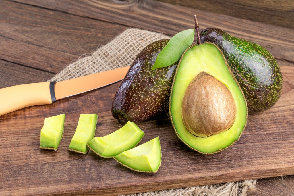 Fresh avocado on cutting board over wooden background