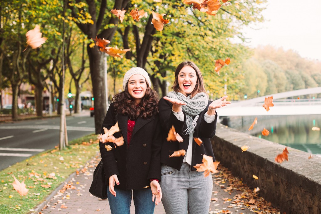 Funny girl friends throwing dry leaves in the city in autumn