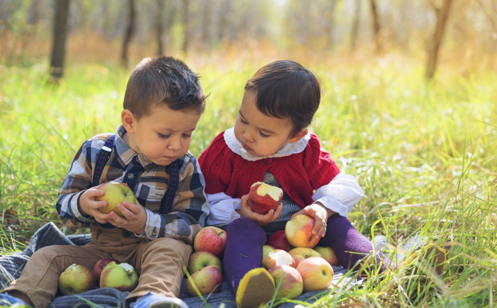two little kids eating apples in the park
