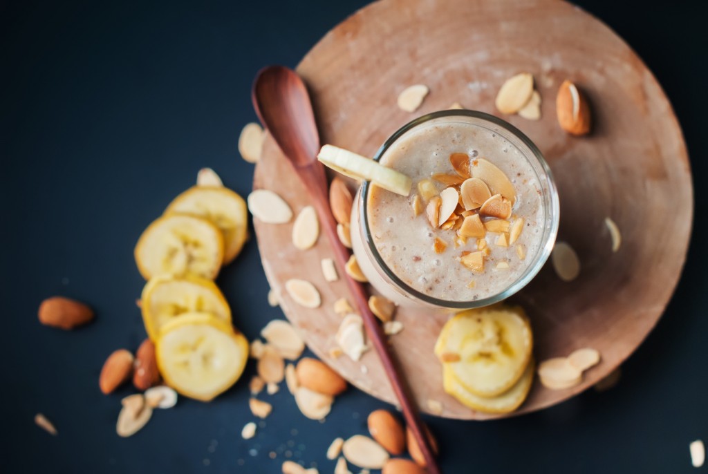 Fruit banana smoothies with milk, almond, flakes, slices of banana on a black chalkboard