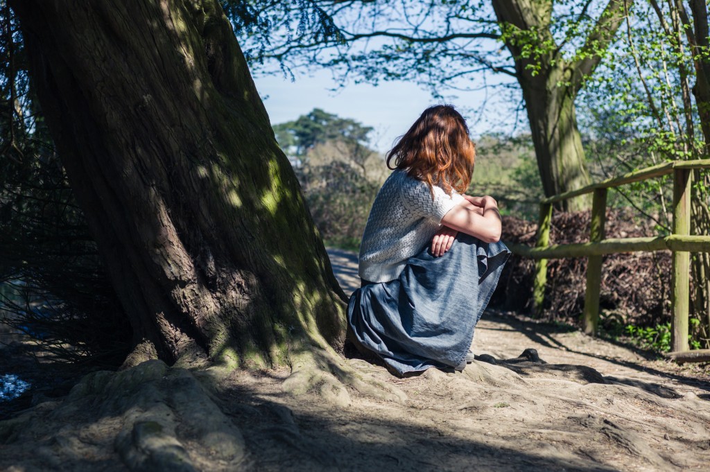 A young woman is sitting under a tree by the water in a forest
