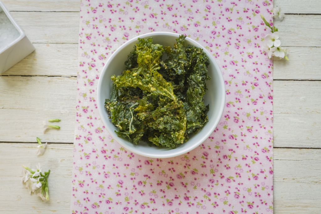 Delicious kale chips on white bowl and pink flowered napkin, ready to enjoy a gourmet snack.